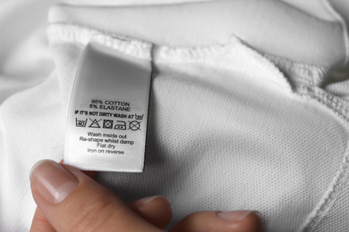 Woman reading clothing label with care symbols and material content on white shirt, closeup