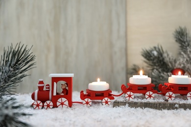 Photo of Red toy train as Christmas candle holder on table with artificial snow in room