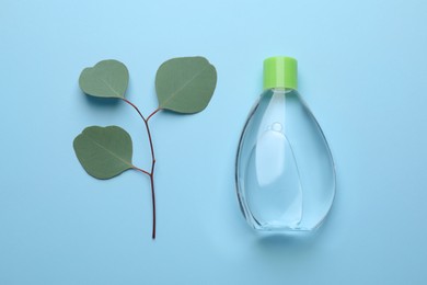 Bottle of baby oil and eucalyptus leaves on light blue background, flat lay