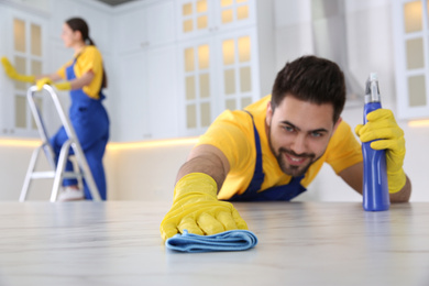 Professional young janitor cleaning table in kitchen