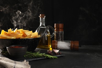 Photo of Composition with bowl of steaming baked potatoes, sauce and spices on black table