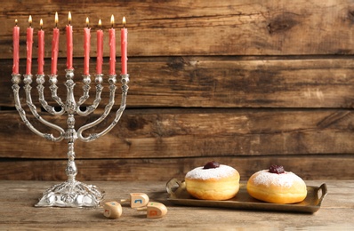 Silver menorah near sufganiyot and dreidels with symbols Nun, He, Pe, Gimel on wooden background, space for text
