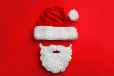 Santa Claus hat with white beard on red background, flat lay