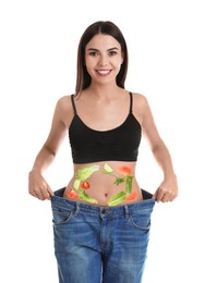 Image of Slim young woman wearing oversized jeans and images of vegetables on her belly against white background. Healthy eating