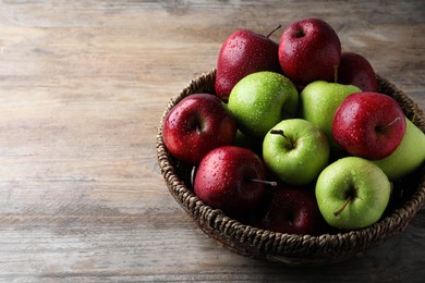 Fresh ripe green and red apples with water drops in wicker bowl on wooden table, space for text