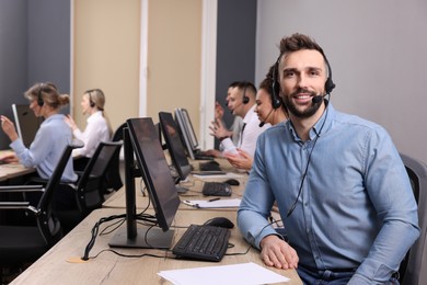 Call center operator with headset and his colleagues working in modern office