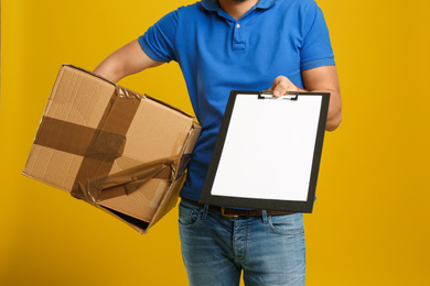 Courier with damaged cardboard box and clipboard on yellow background, closeup. Poor quality delivery service
