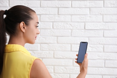 Young woman unlocking smartphone with facial scanner near white brick wall. Biometric verification