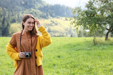 Happy woman with camera on meadow in mountains