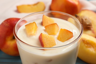 Tasty peach yogurt with pieces of fruit in glass on table, closeup