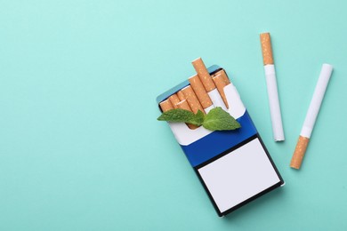 Pack of menthol cigarettes and mint on turquoise background, flat lay. Space for text