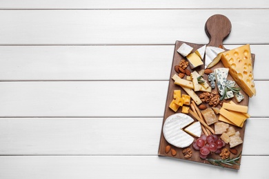 Cheese plate with grapes and nuts on white wooden table, top view. Space for text