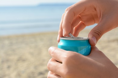 Woman opening aluminum can with beverage on beach, closeup. Space for text