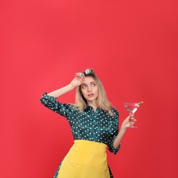 Photo of Young housewife with glass of martini on red background
