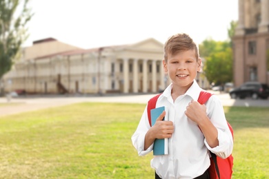 Photo of Little boy with backpack and notebook outdoors. Stationery for school