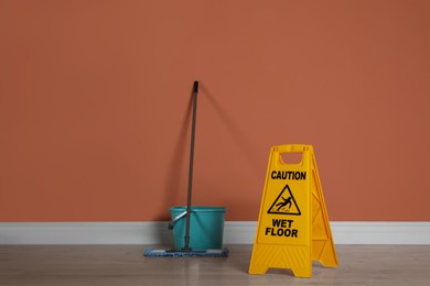Safety sign with phrase Caution wet floor, mop and bucket indoors. Cleaning service