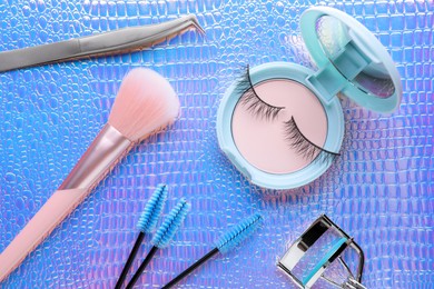 Flat lay composition with false eyelashes and cosmetic products on texture colorful background