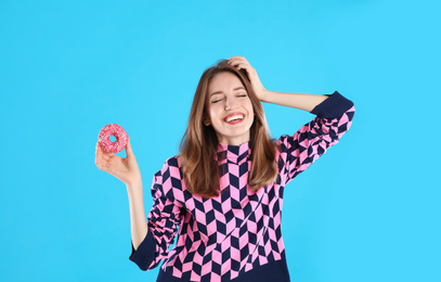 Beautiful young woman with donut on light blue background