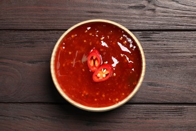 Spicy chili sauce in bowl on wooden table, top view