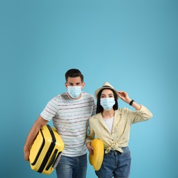 Couple of tourists in medical masks on light blue background. Travelling during coronavirus pandemic