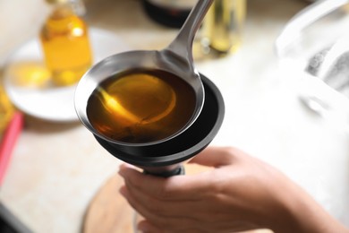 Photo of Woman pouring used cooking oil into bottle through funnel in kitchen, closeup