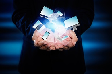 Young businessman holding different devices in hands on color background, closeup 