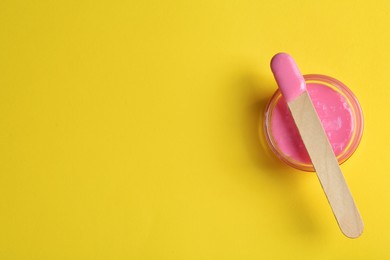Spatula with wax on yellow background, top view. Space for text