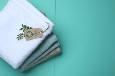 Photo of Stacked towels with recycling label and plant on turquoise background, top view. Space for text