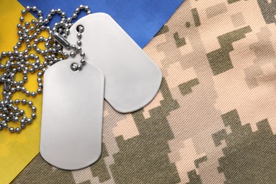 Military ID tags and Ukrainian flag on pixel camouflage, flat lay. Space for text