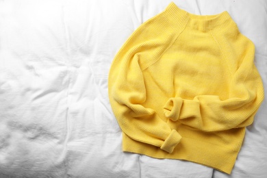 Yellow warm sweater on white bedsheet, top view. Space for text