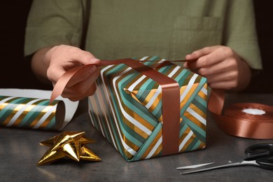 Woman wrapping gift at grey table, closeup