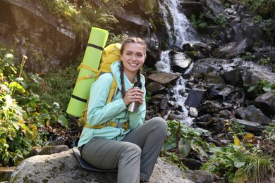 Tourist with vacuum flask near waterfall in mountains