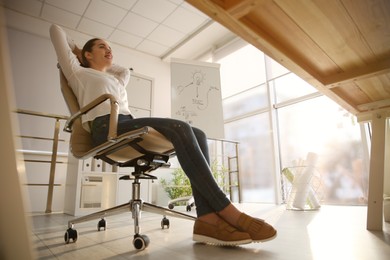 Young woman relaxing in office chair at workplace, low angle view
