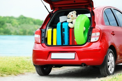 Suitcases, toys and hat in car trunk on riverside