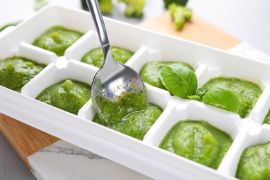 Putting puree with spoon into ice cube tray on table, closeup. Ready for freezing