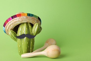 Photo of Wooden maracas, toy cactus with sombrero hat and mustache on light green background, space for text. Musical instrument