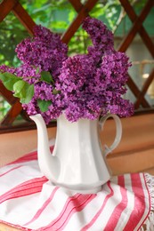 Beautiful lilac flowers in teapot near window indoors