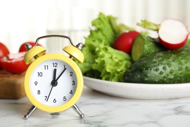 Alarm clock and vegetables on white marble table. Meal timing concept