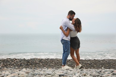 Young couple kissing on beach near sea. Space for text