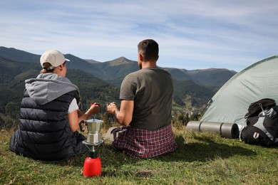 Couple with drinks enjoying mountain landscape near camping tent, back view