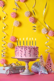 Delicious birthday cake and party decor on pink table against yellow background
