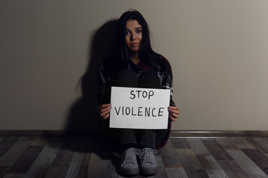 Photo of Abused young woman with sign STOP VIOLENCE near beige wall