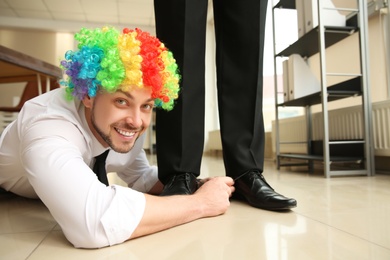 Man with clown wig tying shoe laces of his colleague together in office, closeup. Funny joke