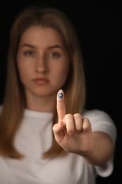 Woman showing finger with drawn blue circle against black background, focus on hand. World Diabetes Day