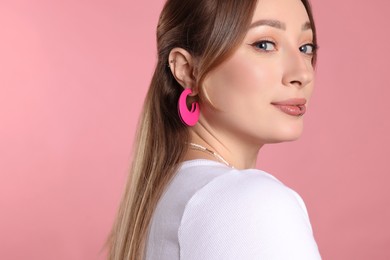 Young woman with lip and ear piercings on pink background. Space for text
