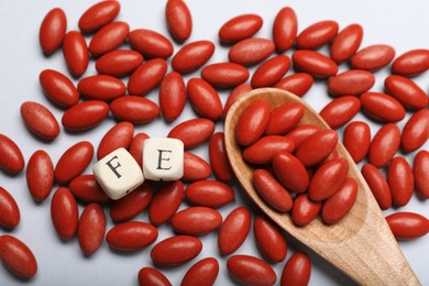Wooden cubes with letters FE, spoon and red pills on white background, flat lay. Anemia treatment
