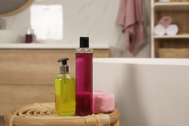 Bottles of shower gels and sponge on wicker table near tub in bathroom, space for text