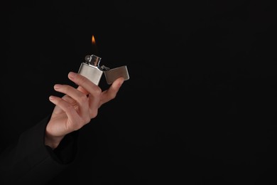 Woman holding lighter with burning flame on black background, closeup. Space for text