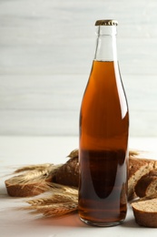 Bottle of delicious fresh kvass, spikelets and bread on white wooden table