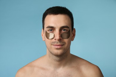 Young man with under eye patches on light blue background
